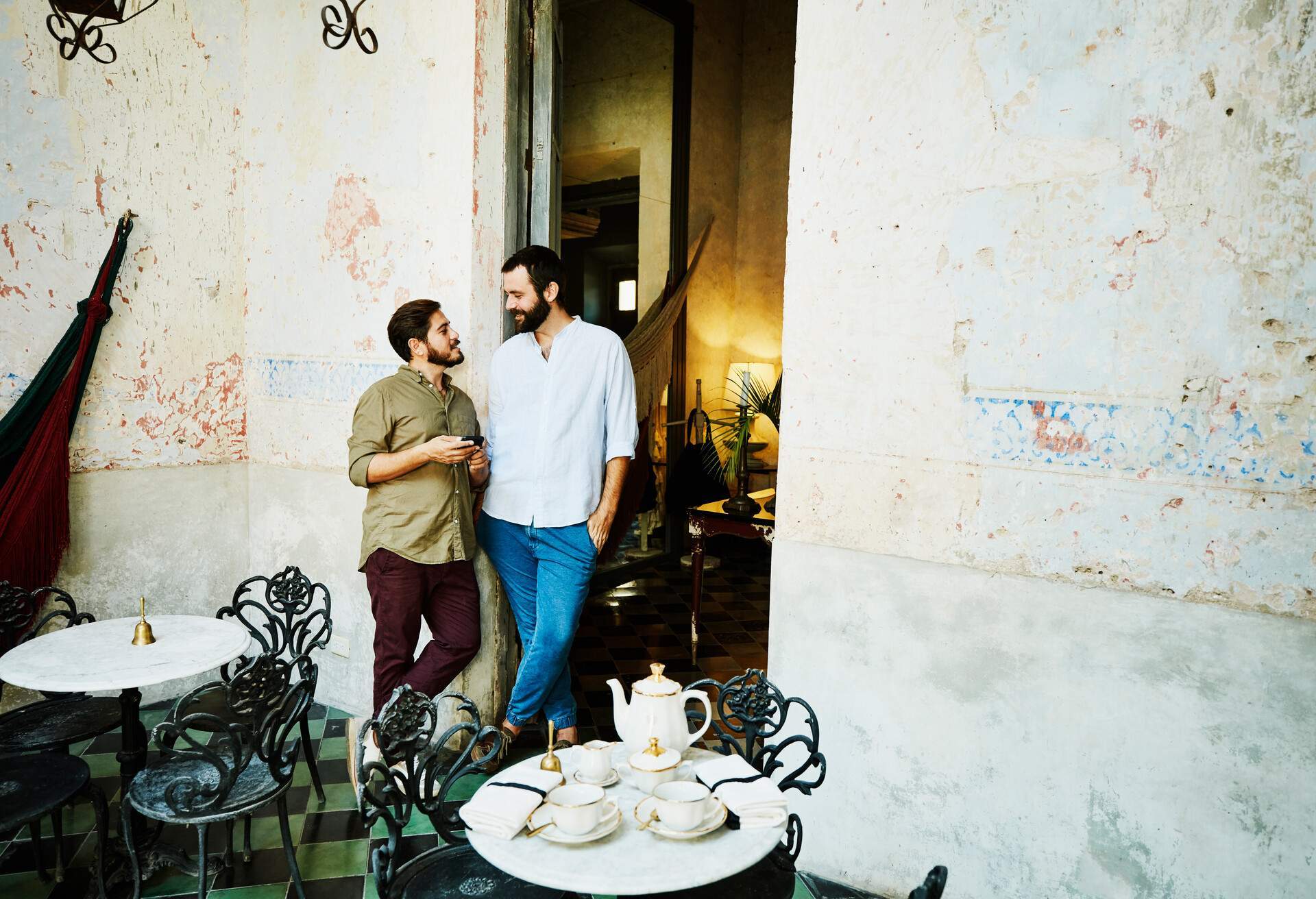 A gay couple leans on the wall of an outdoor cafe.