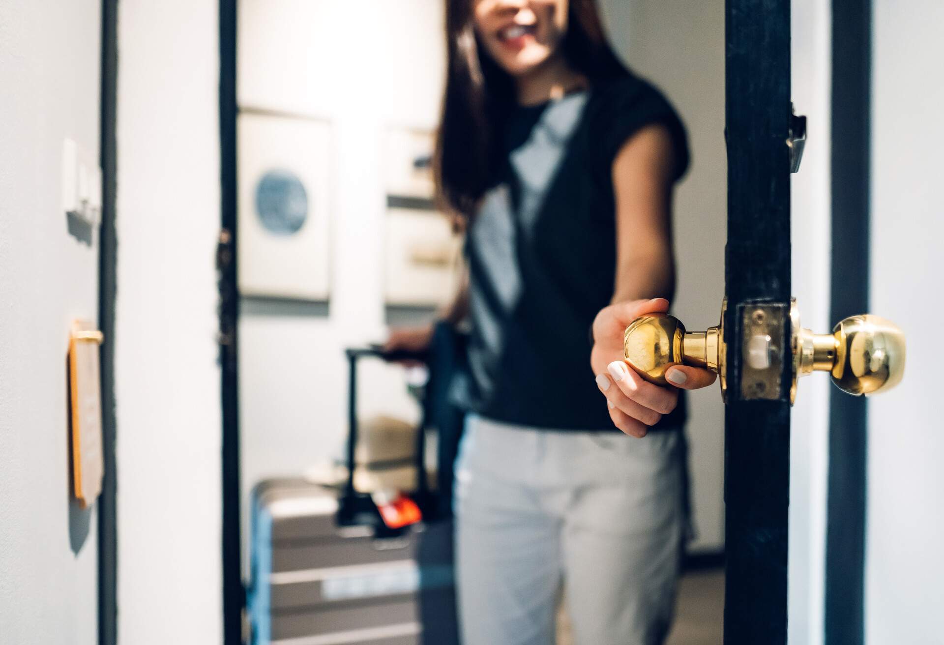 A woman in a black shirt opens a room while grabbing the door knob.
