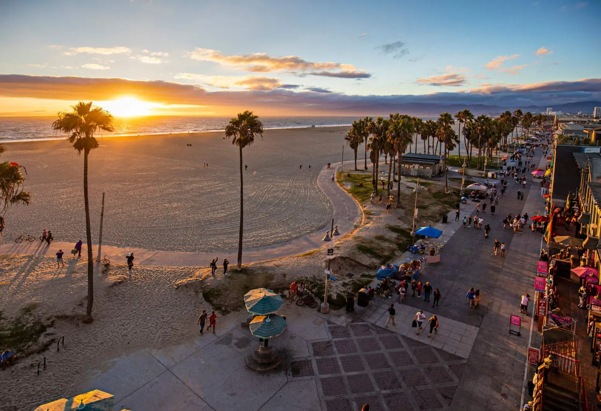 High angle view of Venice beach during sunset. Tourists are walking on footpath by ocean. Shot of beautiful nature and people is taken from above.