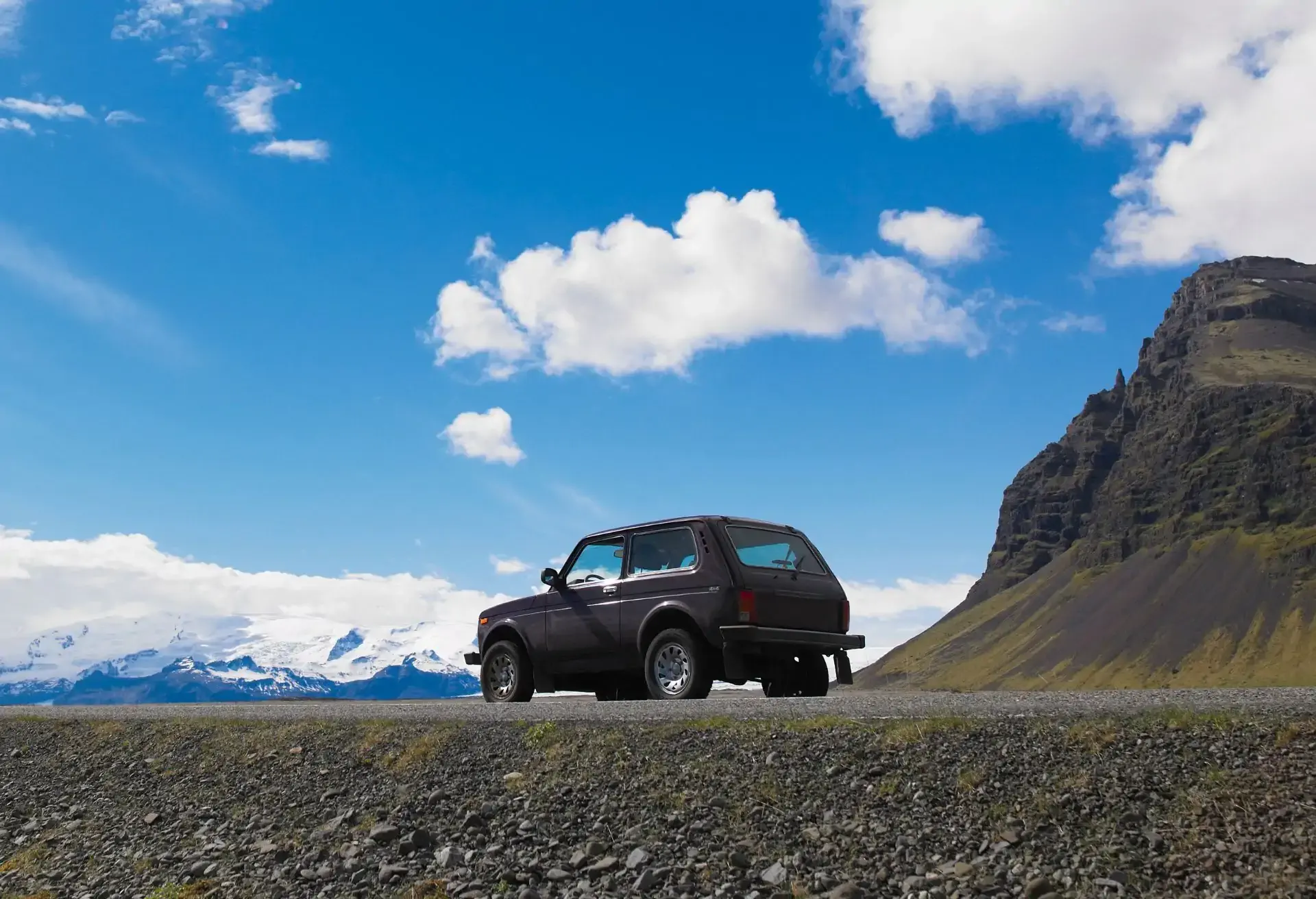 Vehículo SUV negro detenido junto a una carretera con un paisaje de montañas nevadas y cielo azul despejado.