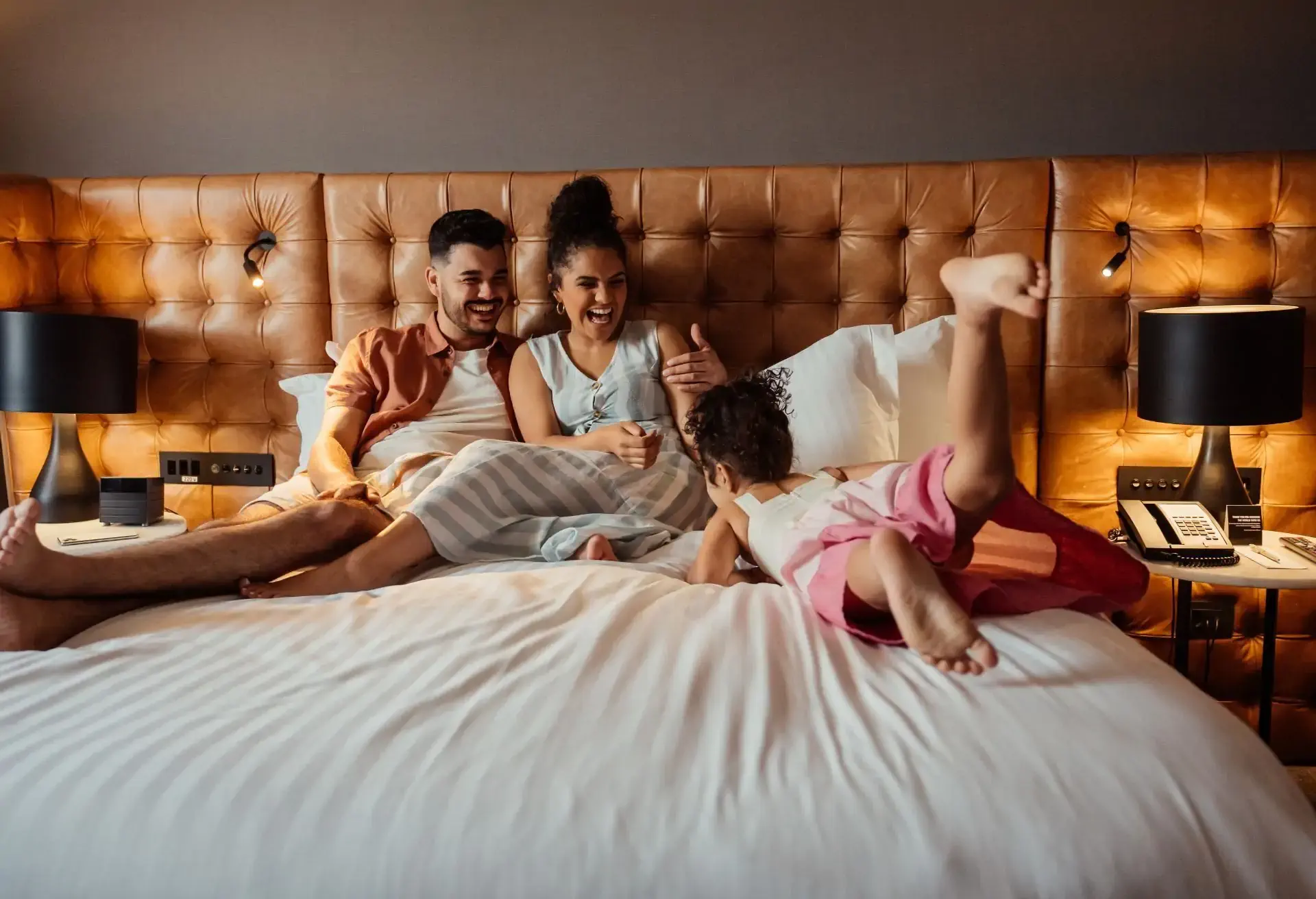 Familia feliz jugando en la cama de una habitación de hotel, transmitiendo momentos de descanso y diversión juntos.