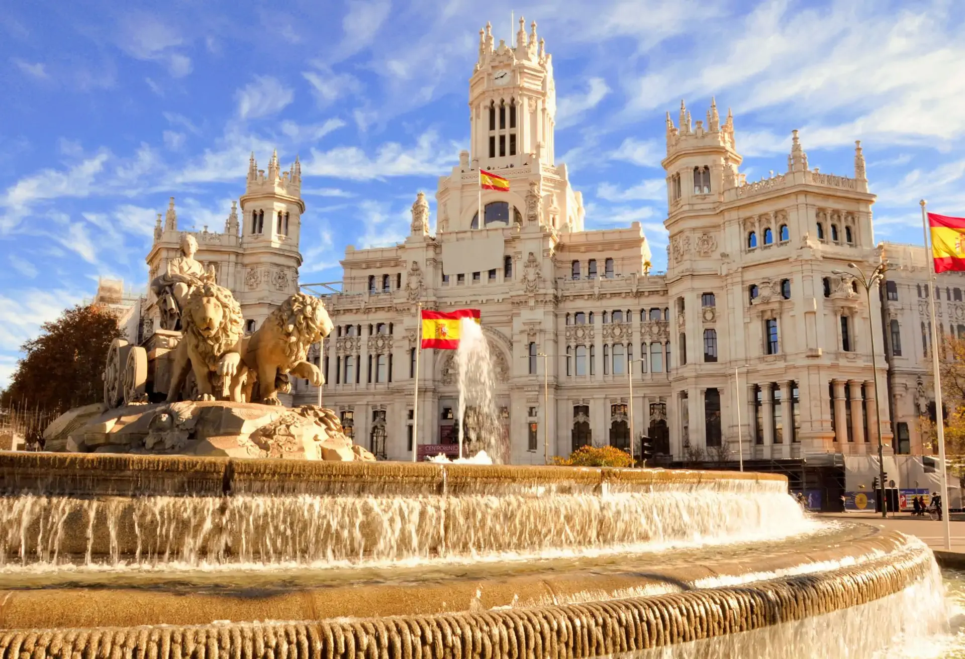 Fuente de Cibeles y Palacio de Cibeles con banderas de España ondeando, anunciando vuelos a Madrid desde $13,699 MXN.
