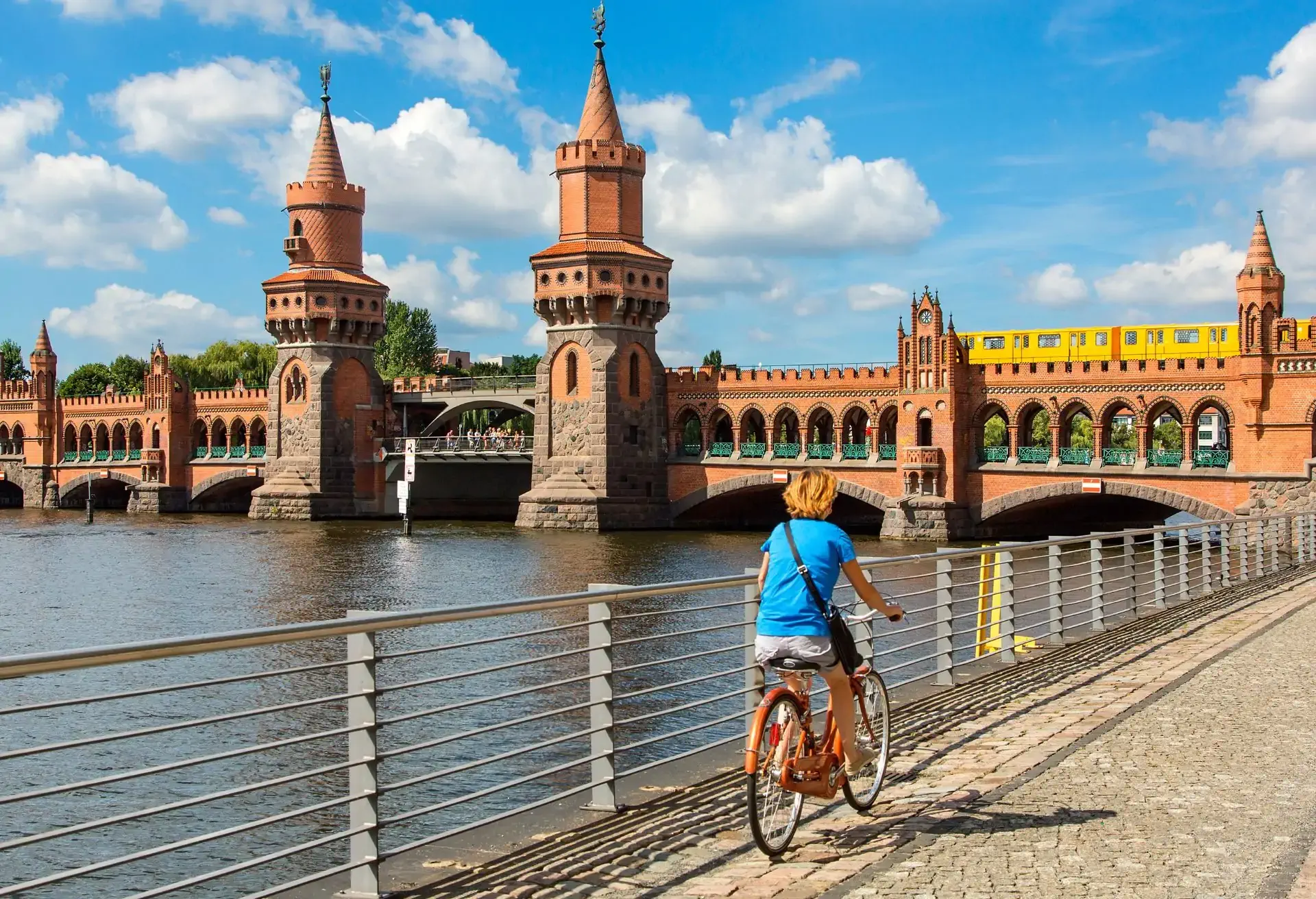 Mujer en bicicleta junto al puente Oberbaum en Berlín, destacando vuelos desde $15,099 MXN hacia la capital alemana.