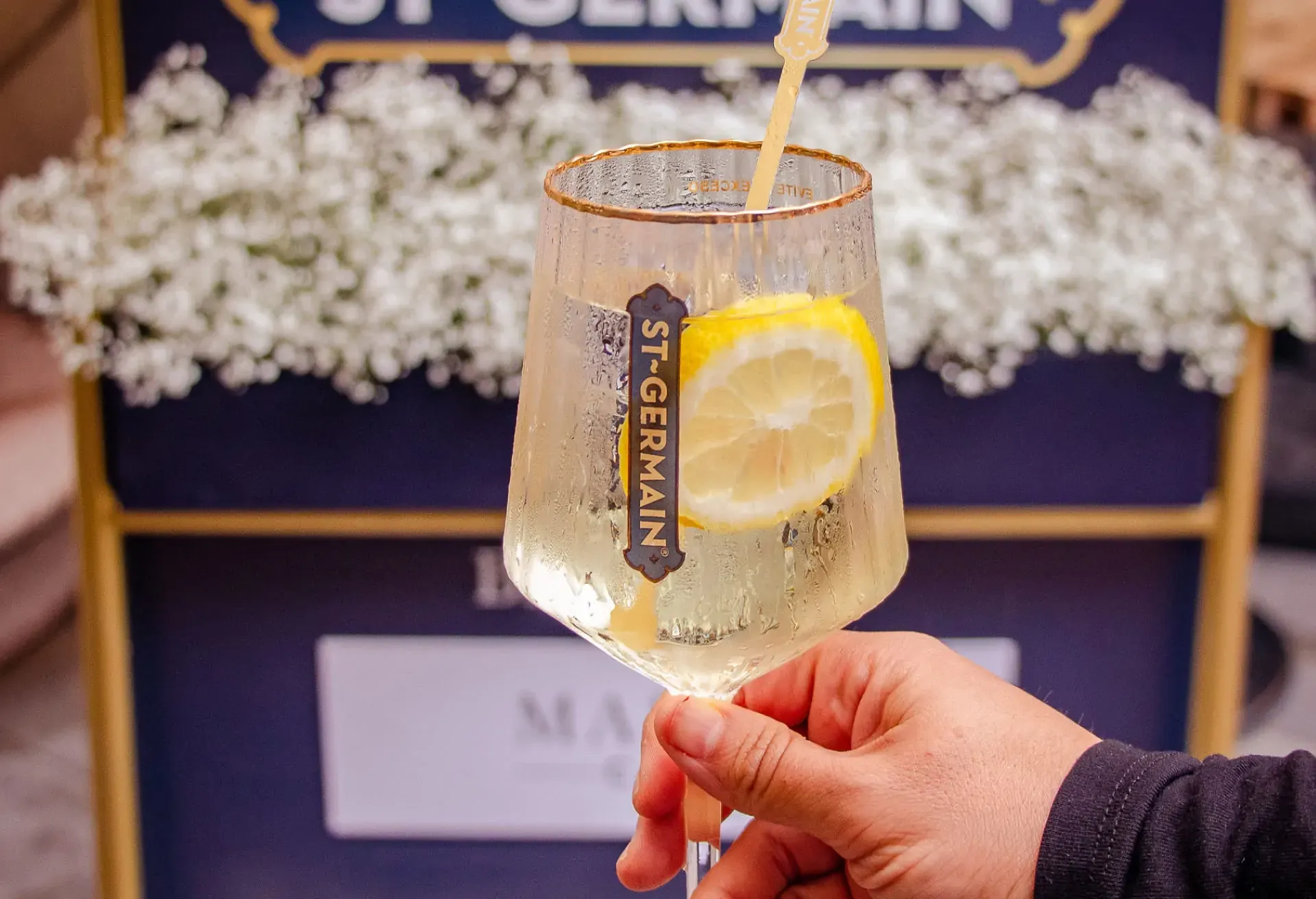 Copa de St-Germain Spritz con rodaja de limón, servida con elegancia en terraza, reflejando el estilo sofisticado de la marca.
