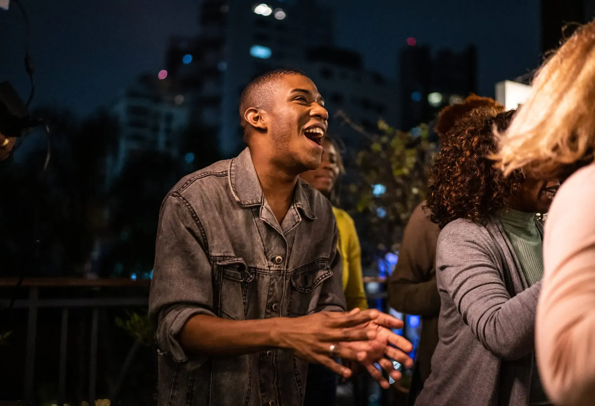 Personas riendo y disfrutando una noche animada en una terraza urbana iluminada.