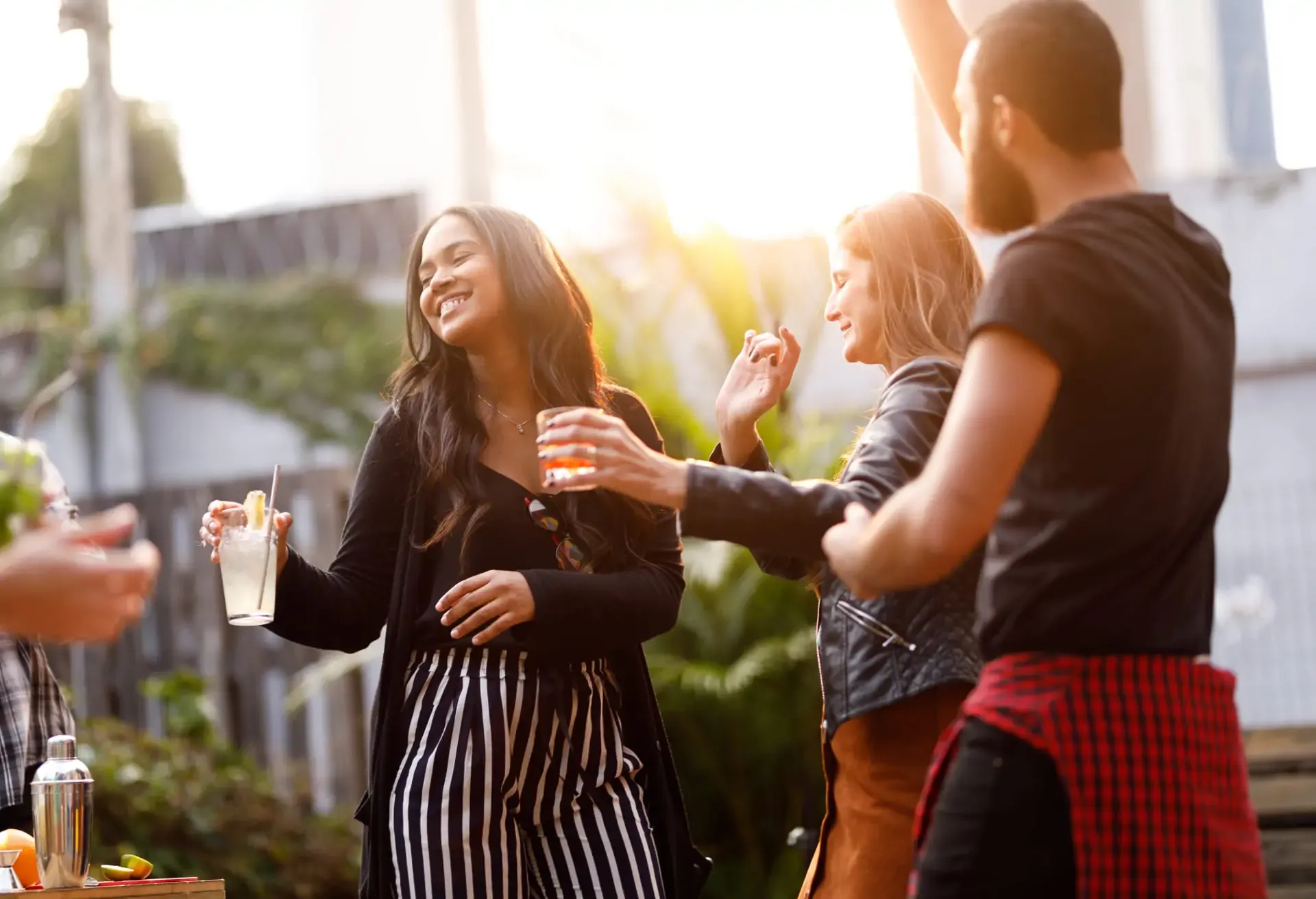 Grupo de personas bailando y disfrutando bebidas al aire libre al atardecer.