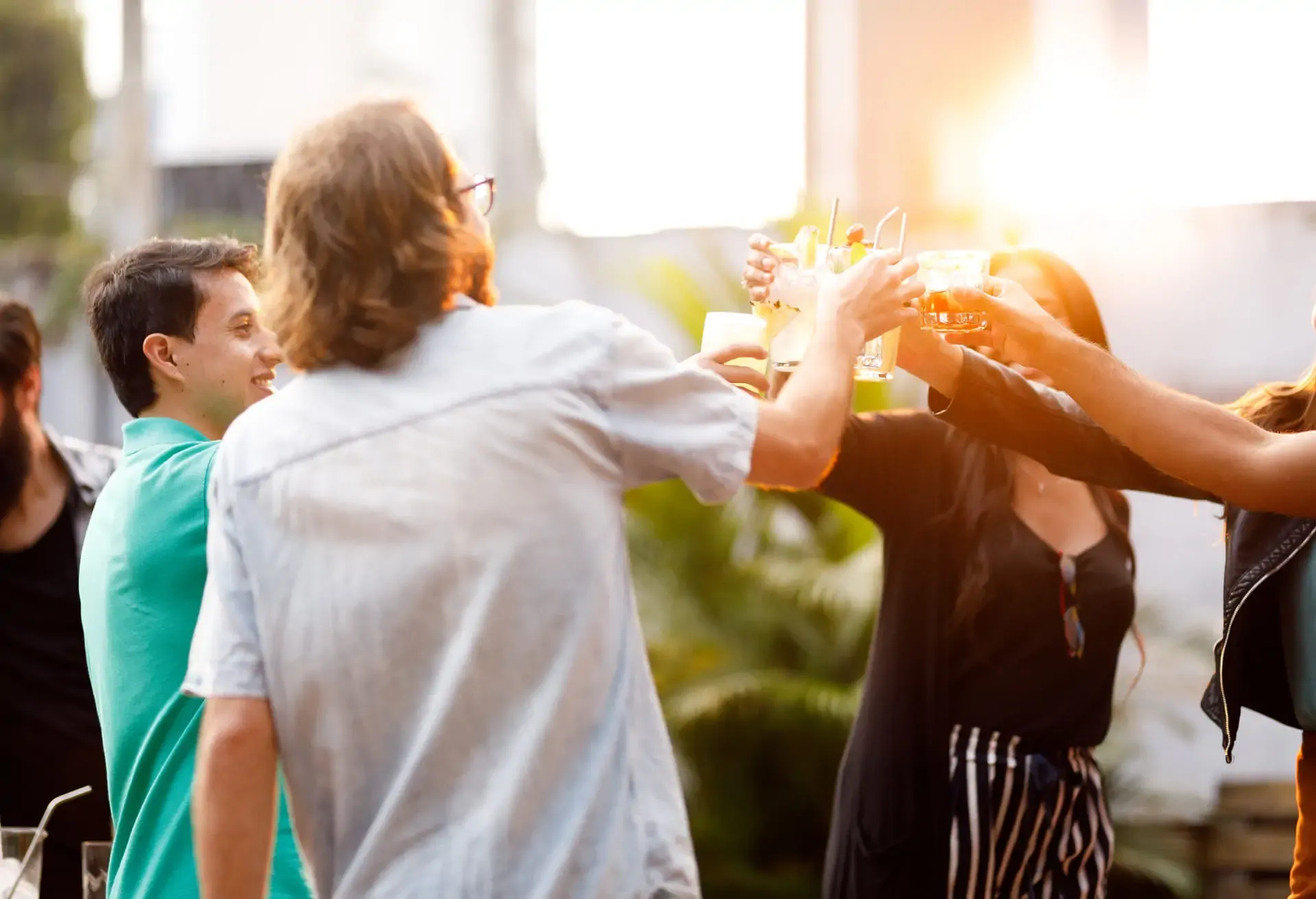 Grupo de personas brindando al aire libre mientras el sol se pone, con ambiente alegre y relajado.
