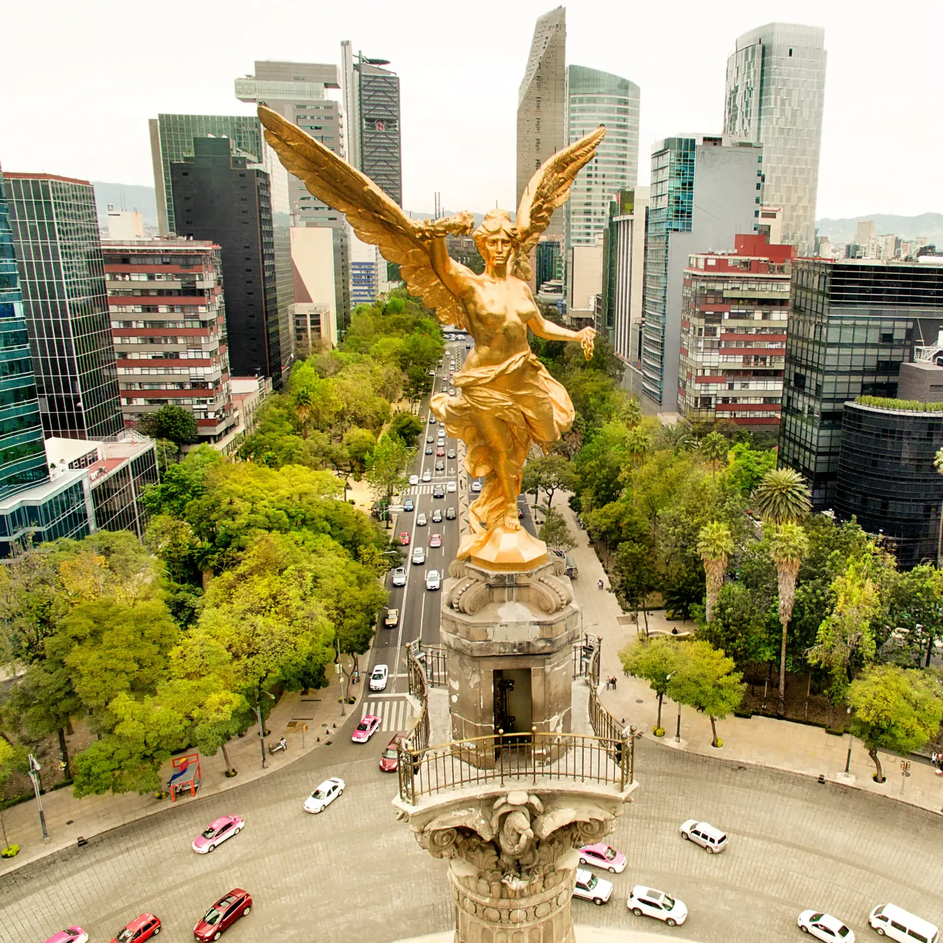 Vista aérea del Ángel de la Independencia en Paseo de la Reforma, Ciudad de México, rodeado de edificios modernos y tráfico en la avenida.