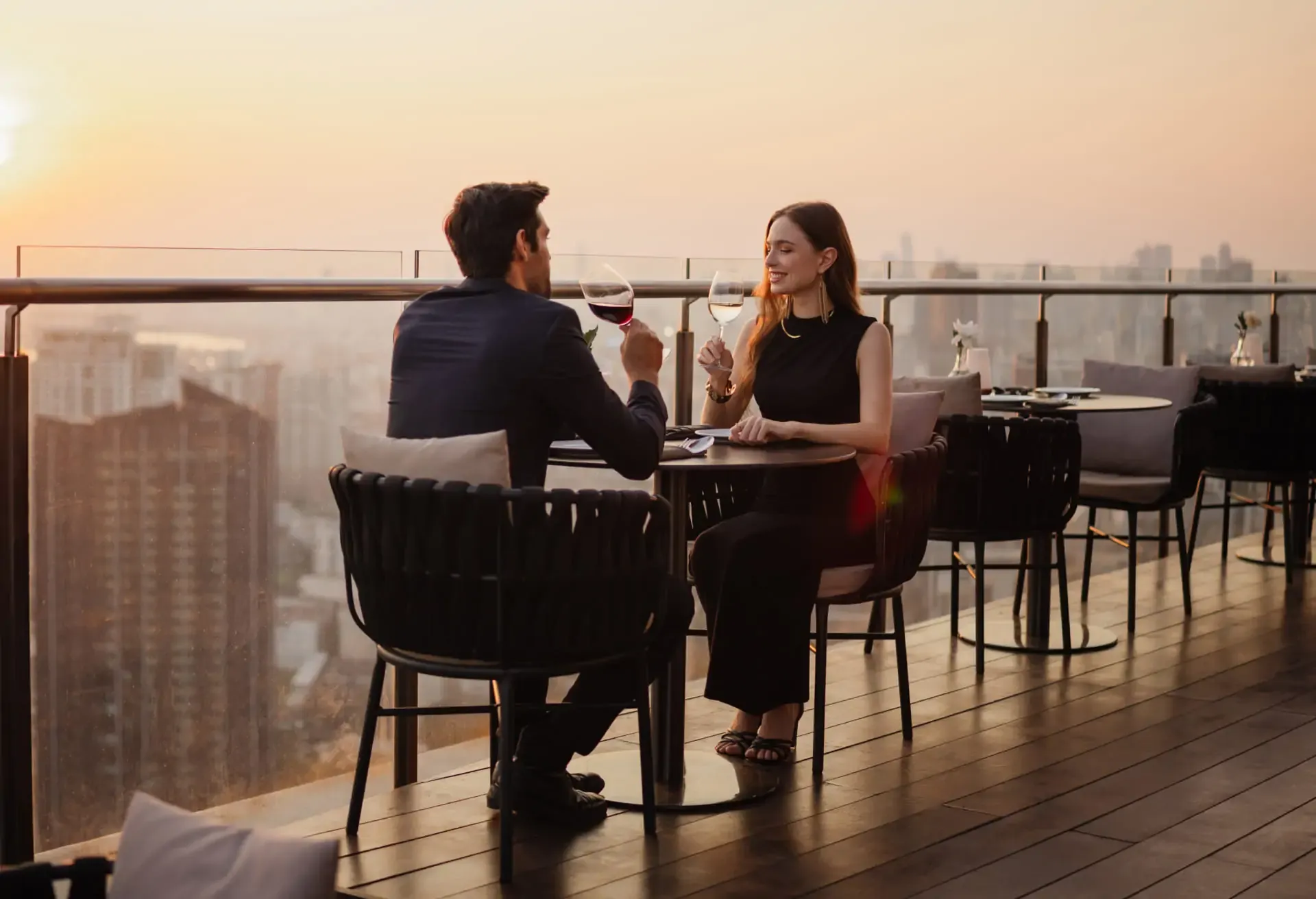 Pareja brindando en una terraza al atardecer con vista panorámica de la ciudad.